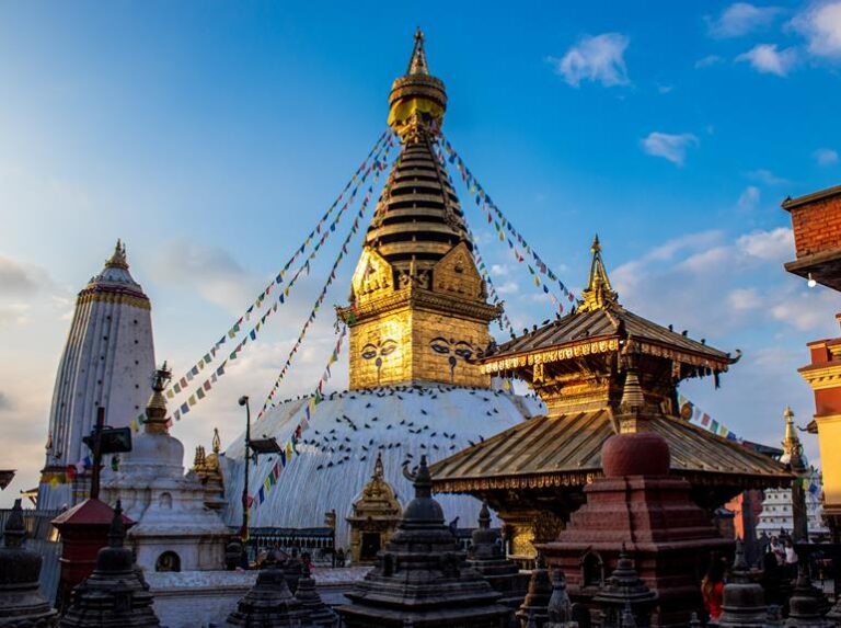 Swayambhunath Stupa, also known as the Monkey Temple in Kathmandu, Nepal, under a clear blue sky with prayer flags radiating from the central golden spire decorated with the iconic Buddha eyes.