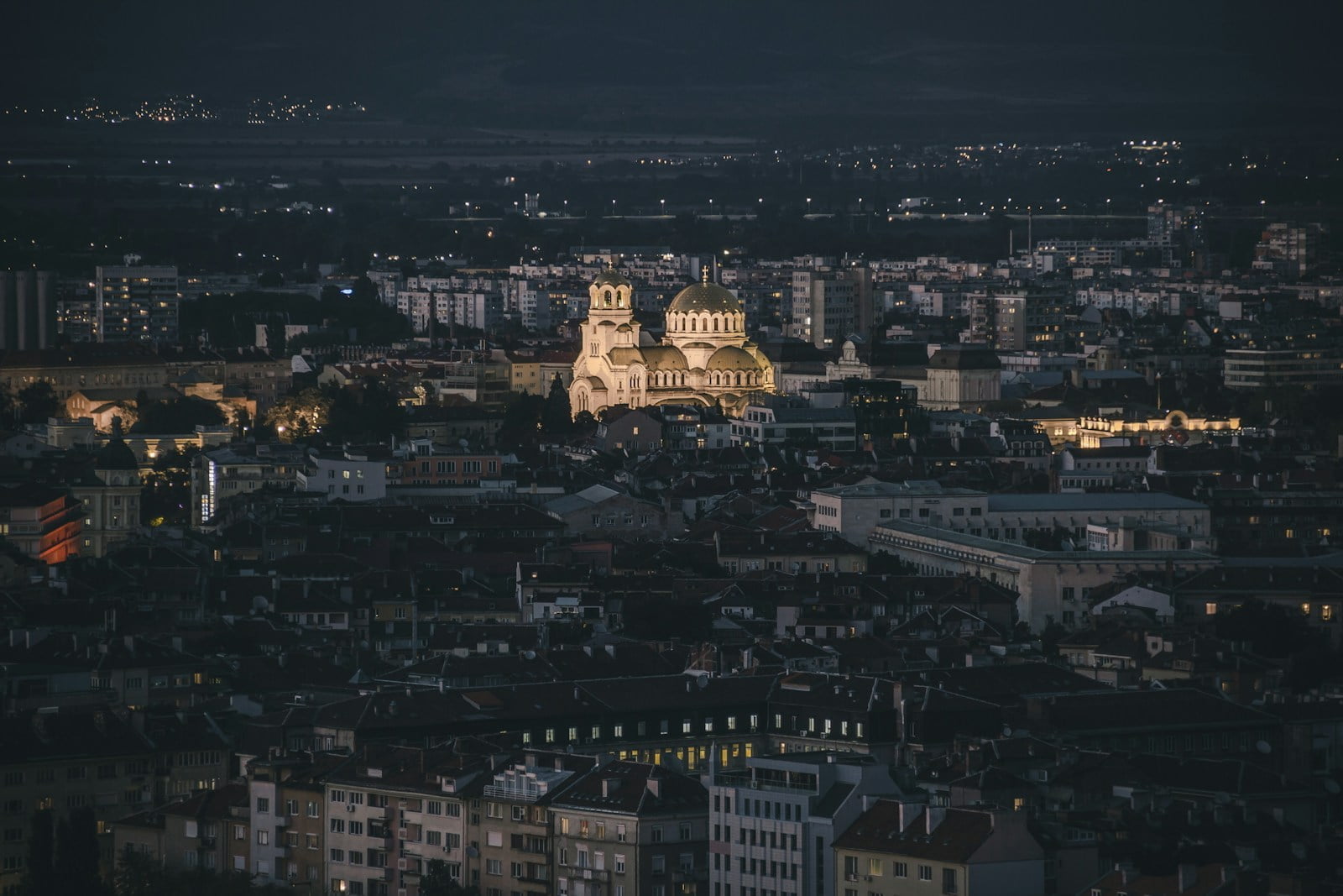 A night view of a cityscape with illuminated buildings and a prominently lit cathedral standing out against the dark sky.