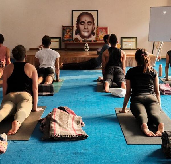 People practicing yoga in a studio with a large portrait on the wall in the background and yoga mats on the floor.