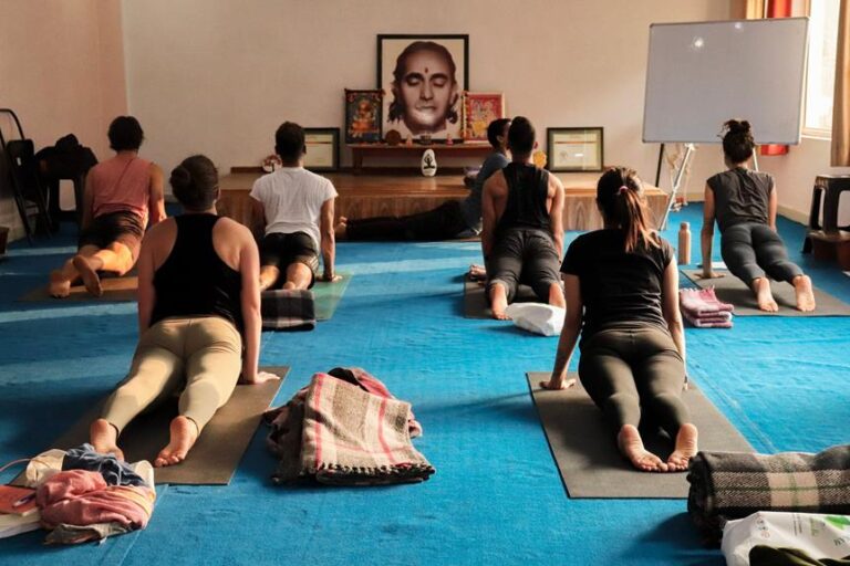 People practicing yoga in a studio with a large portrait on the wall in the background and yoga mats on the floor.